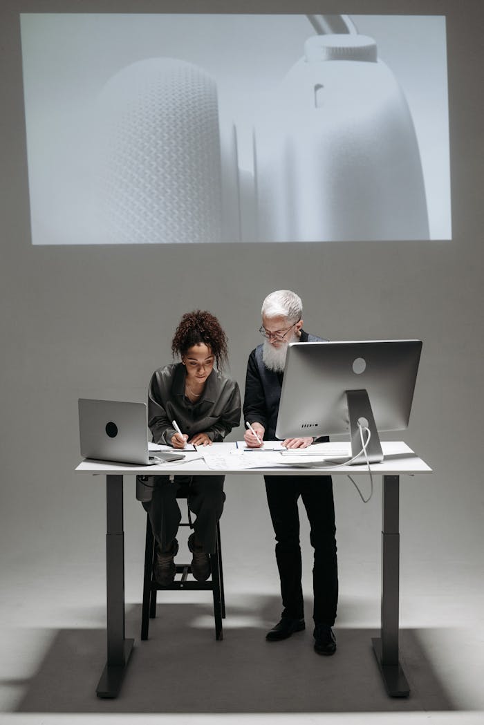 Two professionals collaborate in a high-tech setting with laptops and digital screens.